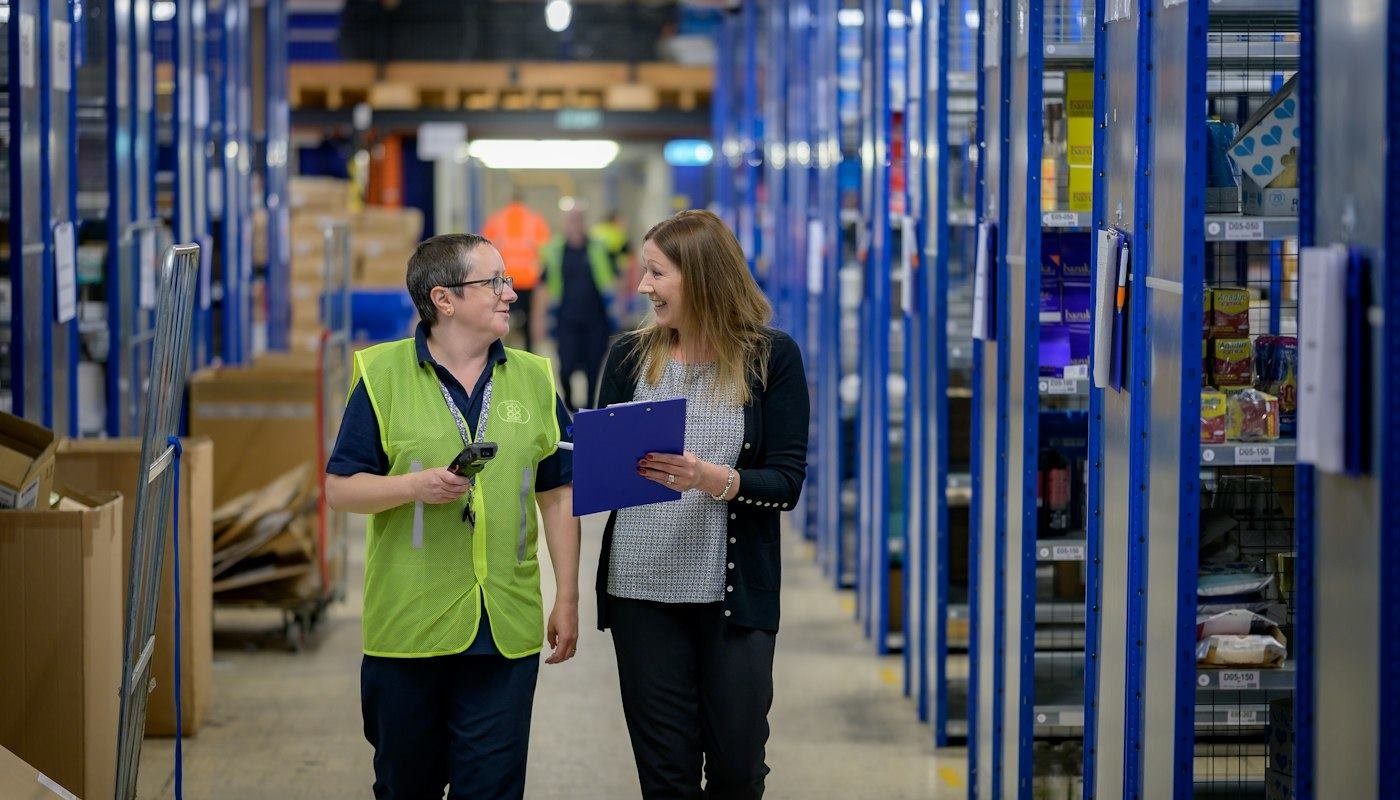 Two colleagues reviewing stock together in a warehouse aisle